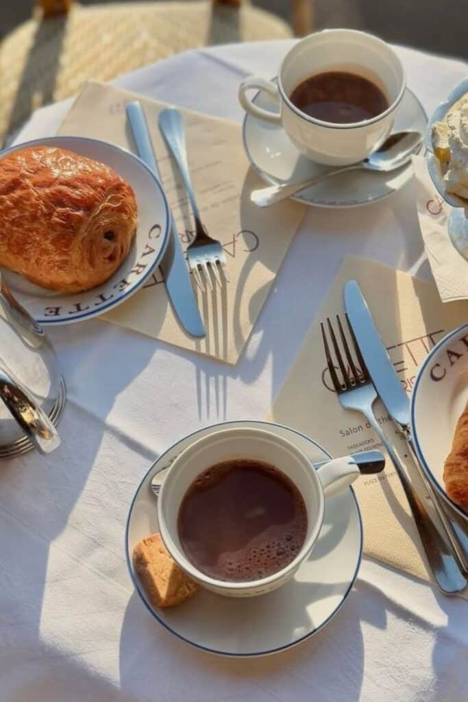 A sunlit table at Carette in Paris, featuring two cups of the best hot chocolate in Paris, served with buttery pastries and crisp tableware.