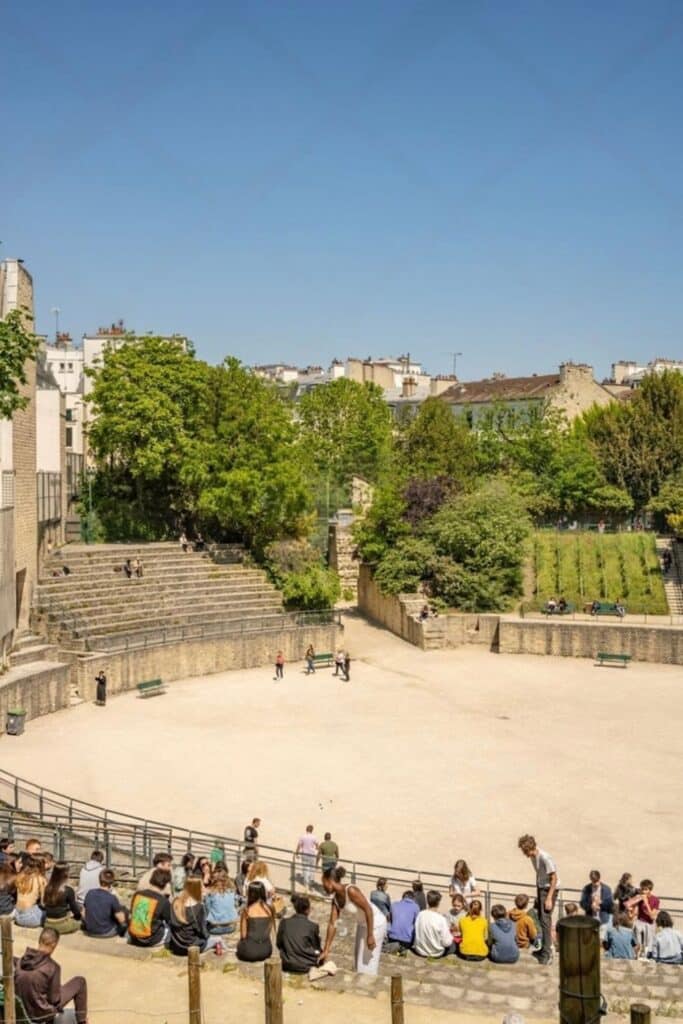 People sitting on the ancient stone terraces of Arènes de Lutèce, a Roman amphitheater tucked away in Paris, one of the hidden gems in Paris where locals gather to relax and enjoy the historic site.