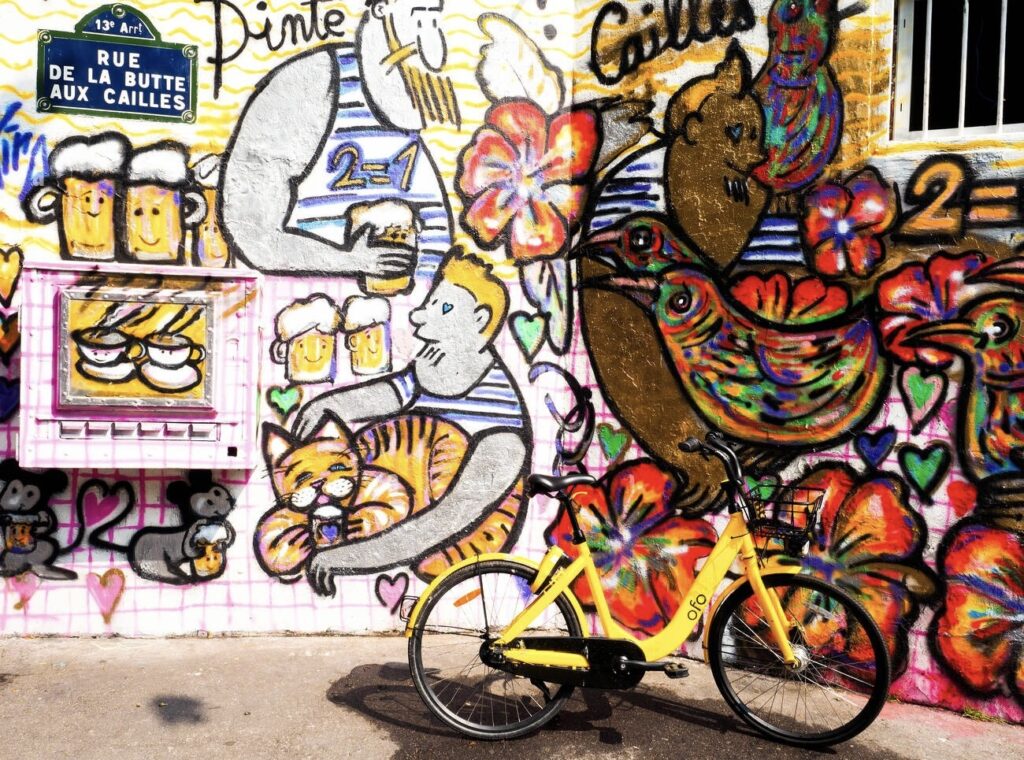 Colorful street art mural in Butte-aux-Cailles, featuring playful cats, birds, and beer mugs, with a yellow bicycle parked in front—one of the hidden gems in Paris known for its creative graffiti and village-like charm.