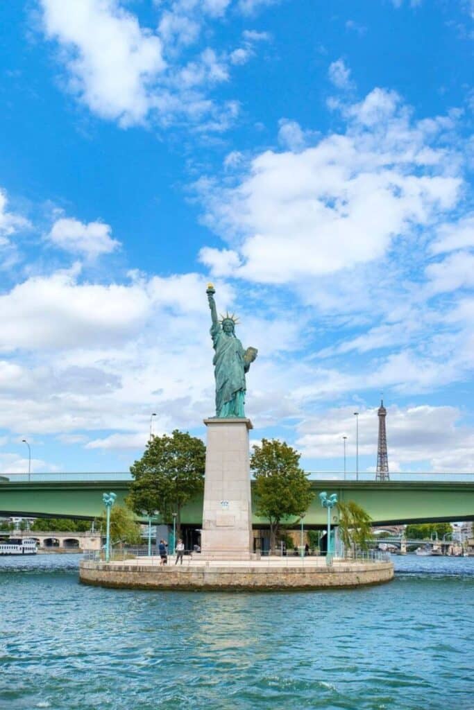 Statue of Liberty replica on Île aux Cygnes along the Seine River, with the Eiffel Tower in the background, one of the hidden gems in Paris that surprises visitors with its New York connection and peaceful riverside views.