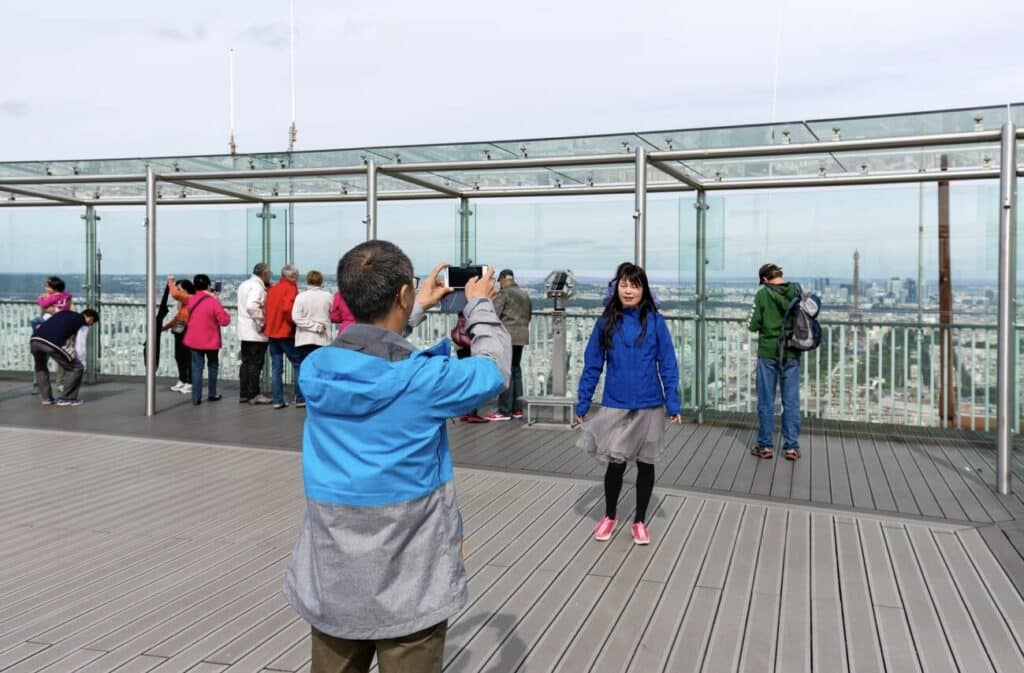 Tourists enjoying panoramic views of Paris from the Montparnasse Tower observation deck, one of the hidden gems in Paris for stunning cityscape views and a unique perspective of the Eiffel Tower.