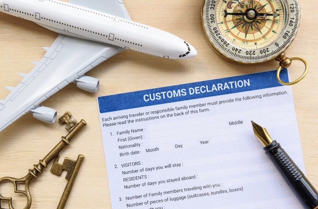 A customs declaration form placed alongside a model airplane, a vintage key, and a compass, symbolizing travel and possibly returning with Marseille souvenirs.