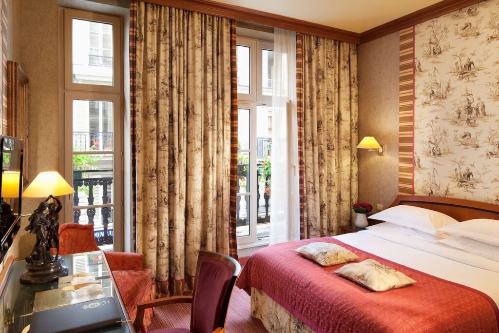 Cozy and classic bedroom at Paris Hotels with Connecting Rooms featuring patterned curtains, warm lighting, and traditional décor.