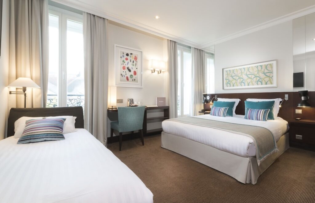 Bright and modern room with a double bed and single bed at Paris Hotels with Connecting Rooms, featuring colorful pillows and a workspace.