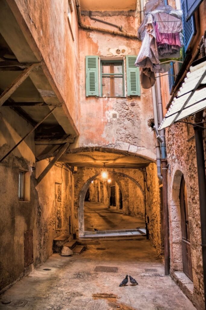 Rue Obscure in Villefranche-sur-Mer, a historic covered passageway with weathered walls and dim lighting that creates an air of mystery. Laundry hangs from a window above, adding a touch of daily life to this intriguing walkway, a hidden gem for those discovering things to do in Villefranche-sur-Mer.