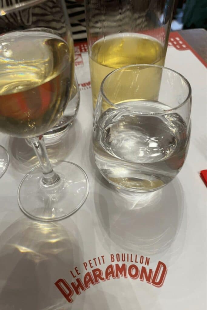 Close-up of drinks at Le Petit Bouillon Pharamond, a historic spot among bouillon restaurants in Paris, featuring wine, beer, and water on a branded placemat.