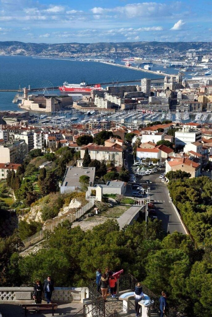 A panoramic view from the Notre-Dame de la Garde Basilica, overlooking the bustling cityscape and port of Marseille with the Mediterranean Sea extending to the horizon, a must-visit spot to take in during 'one day in Marseille'.