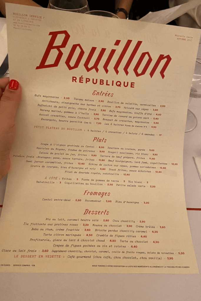 Hand holding the autumn menu at Bouillon République, highlighting the diverse entrée, plat, and dessert options found in classic bouillon restaurants.