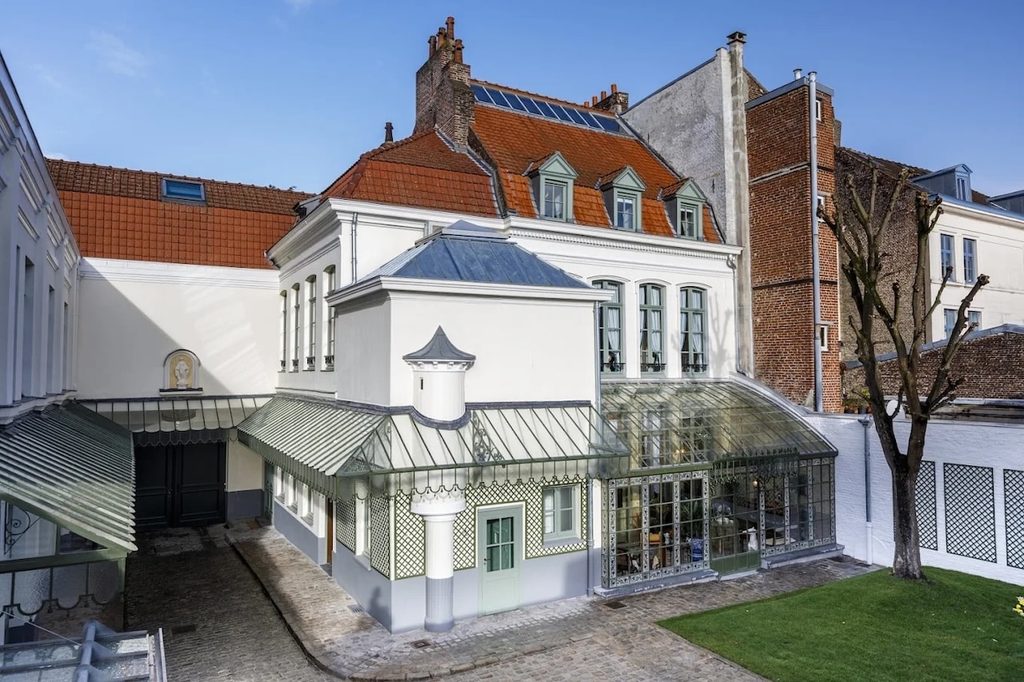 Exterior of Charles de Gaulle’s birthplace museum in Lille, showing the historic brick townhouse, tall windows, arched entrance, and French flags along Rue Princesse.