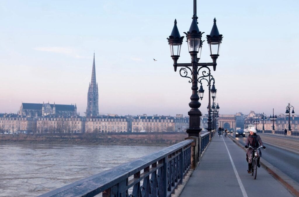 A tranquil winter morning on Pont de Pierre with locals commuting by bicycle, overlooking the frost-touched skyline of Bordeaux, capturing the city’s calm elegance in the winter.