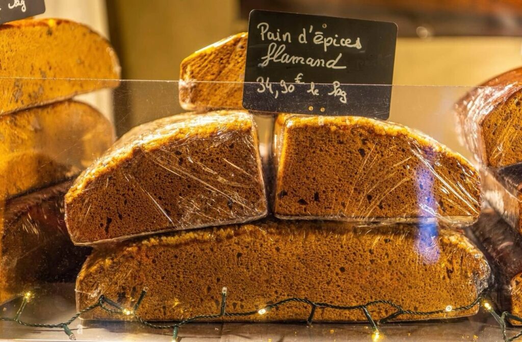Slices of traditional Pain d'épices Flamand, a gingerbread-like cake, priced at 3.90 euros per 100 grams, showcased at a Lille Christmas market, wrapped and ready for festive indulgence.
