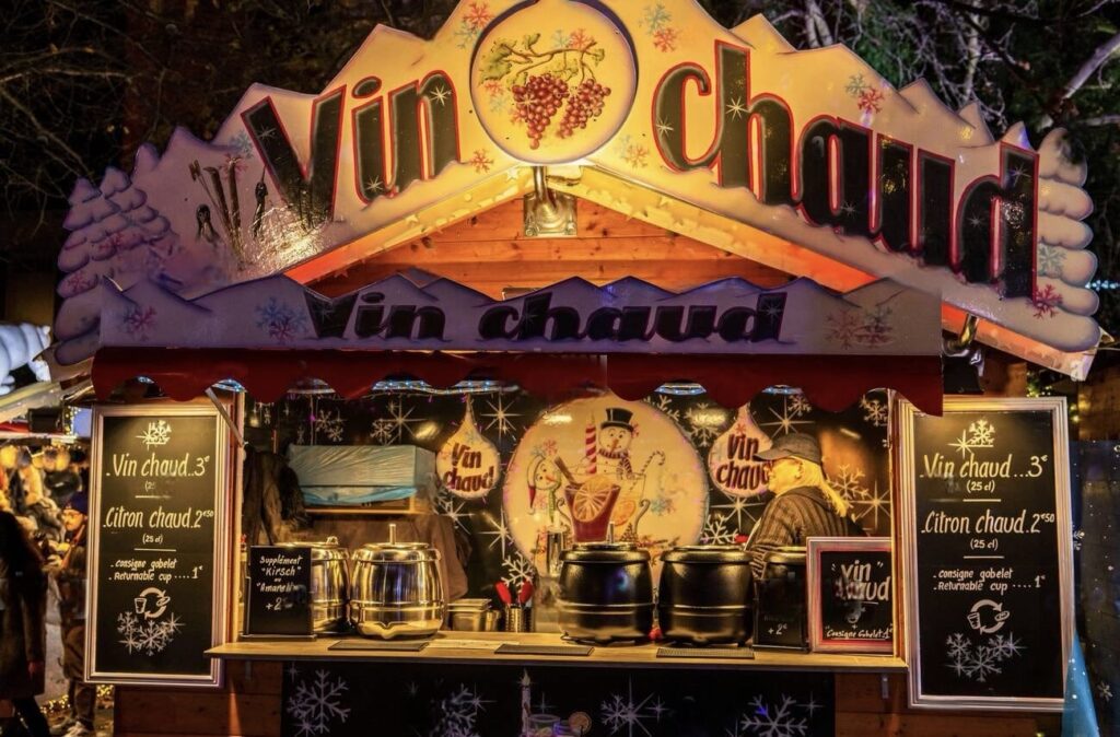 A cozy 'Vin Chaud' stall at the Lille Christmas Market, offering hot mulled wine and lemon, with a warm and festive ambiance, inviting visitors to enjoy traditional winter beverages.