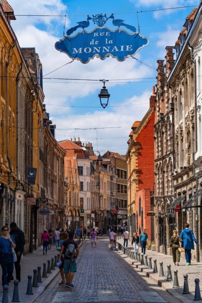 A cobblestone street in Lille, France, lined with historic buildings, pedestrians, and a "Rue de la Monnaie" sign overhead, showcasing one of the popular things to do in Lille.