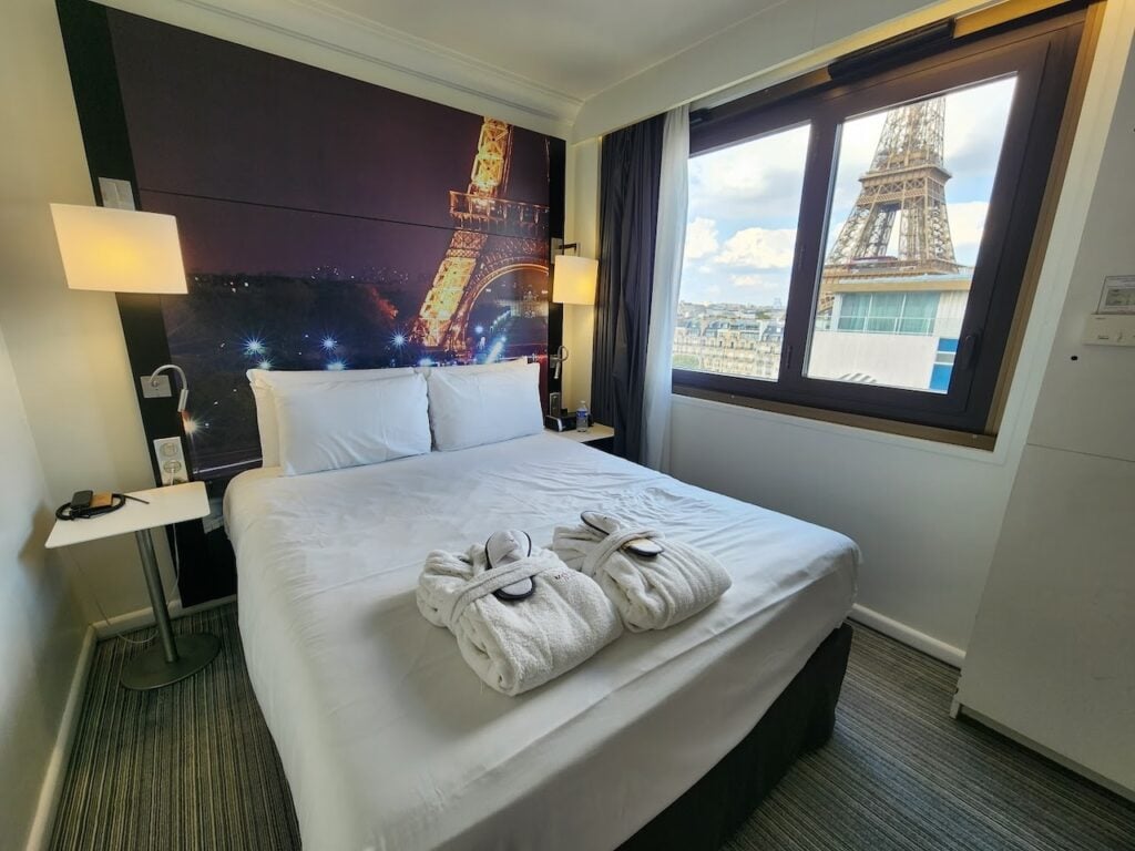 Bright room at Mercure Paris Centre Eiffel Tower with a comfortable bed, robes, and a window offering a clear view of the Eiffel Tower, perfect for cheap hotels with Eiffel Tower view.