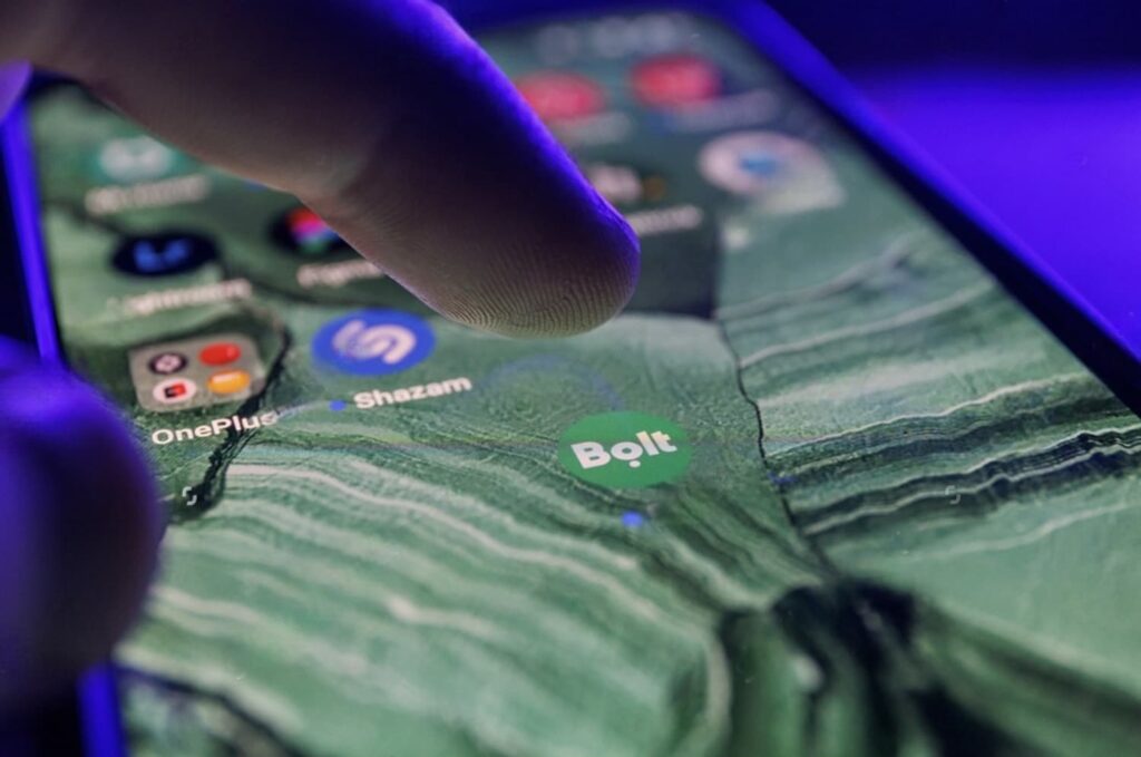 Close-up of a person's finger about to tap the 'Bolt' app on a smartphone screen, with the app's interface showing a map in the background, and other app icons like 'OnePlus' and 'Shazam' visible.