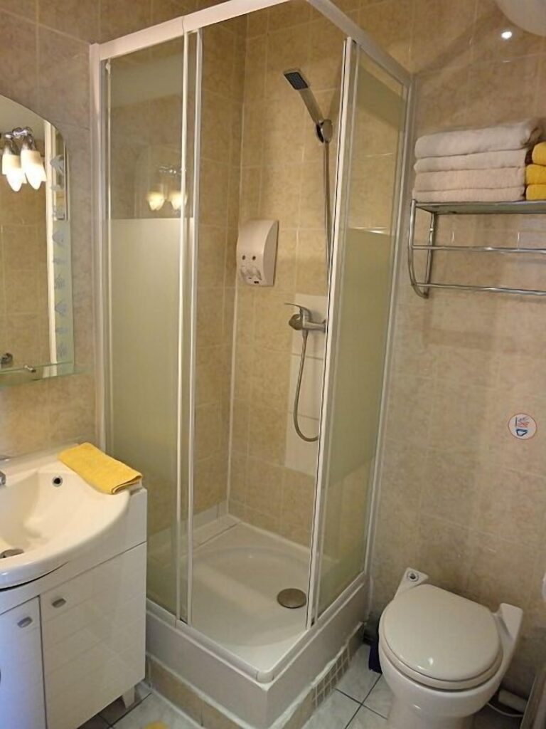 A neatly organized bathroom featuring a corner shower with glass doors, a white sink with a vanity unit, a toilet, and neatly stacked towels on a wall-mounted rack.