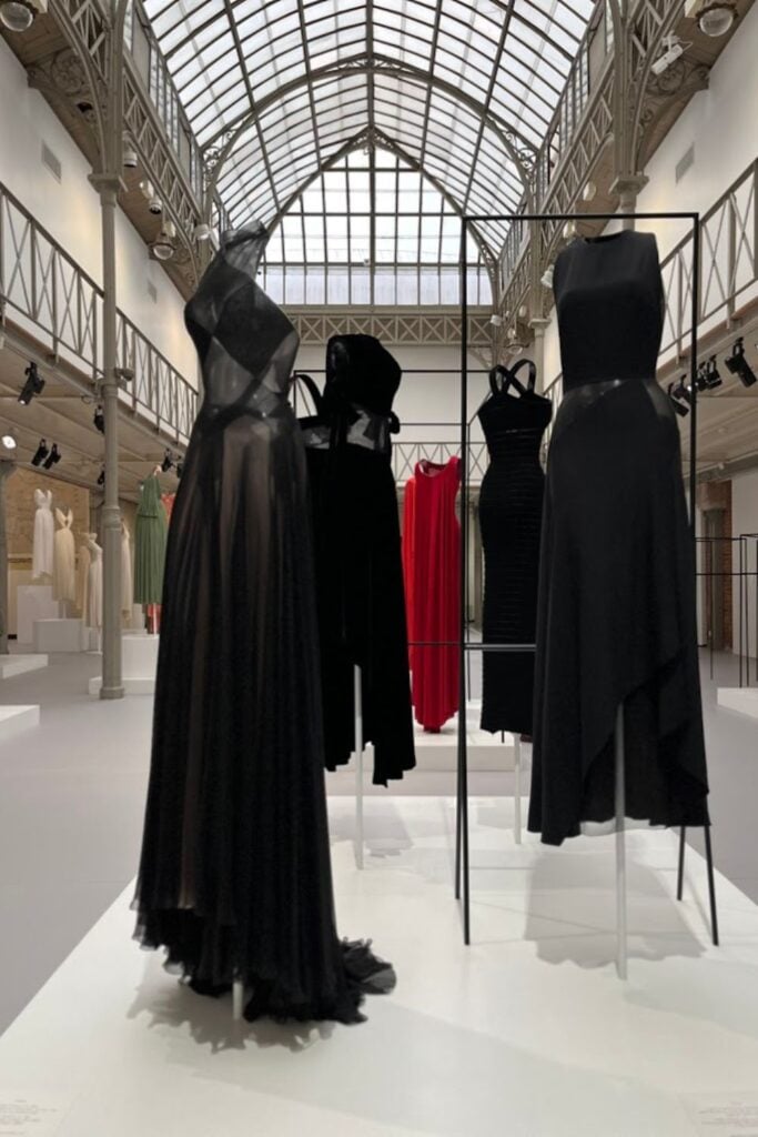 Mannequins displaying elegant black and red dresses under the ornate glass ceiling of one of the best fashion museums in Paris.