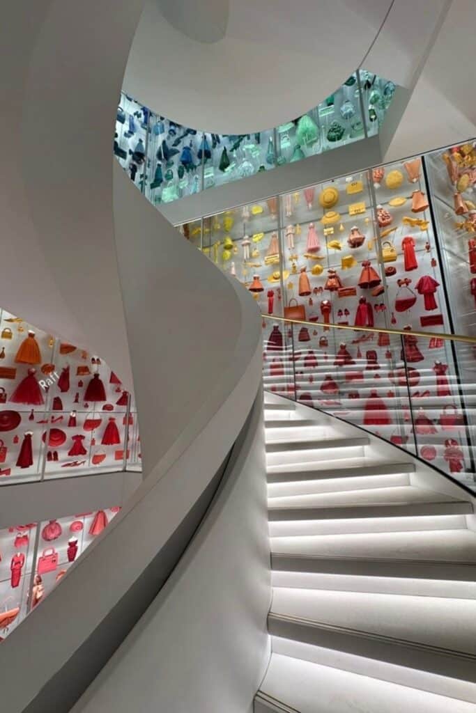 A spiraling white staircase leads past colorful displays of miniature dresses and accessories in one of the best fashion museums in Paris.