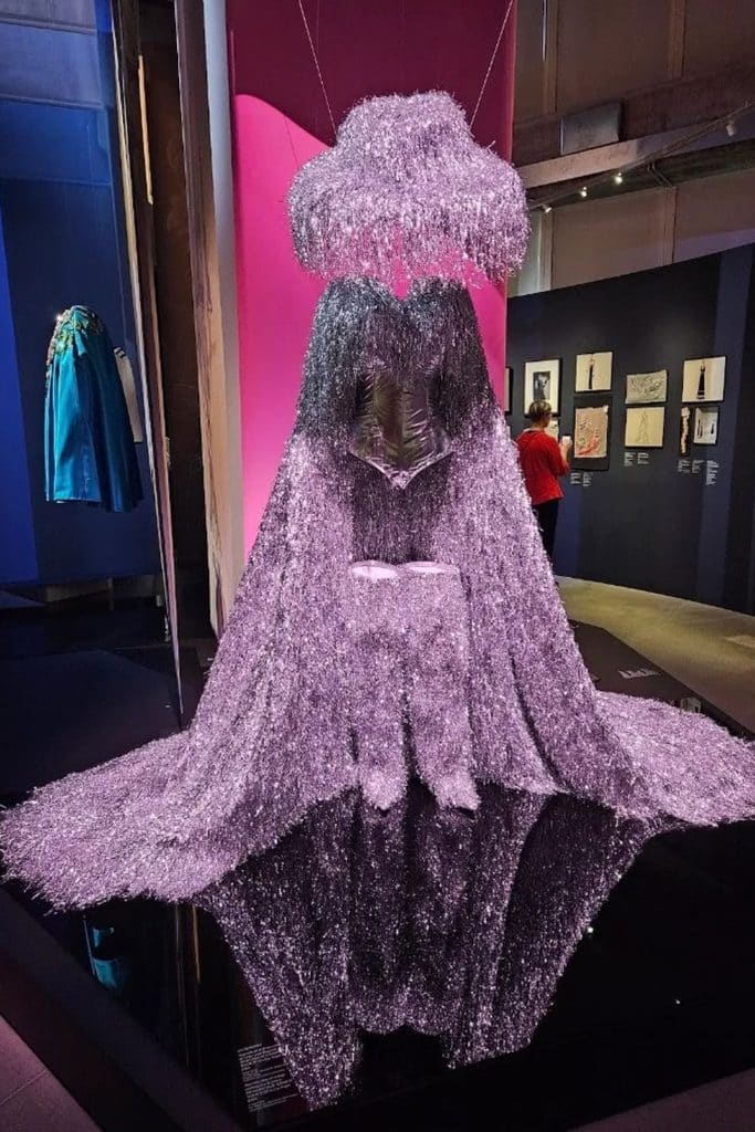 Dramatic silver fringed fashion design with a black corset displayed beneath pink lighting at Galerie du 19M in Paris.