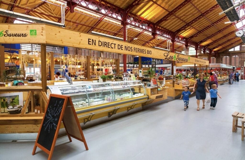Marché Couvert de Colmar, a vibrant covered market featuring wooden stalls selling fresh produce, cheeses, and local specialties. Shoppers browse the selection of organic farm products under the beautifully restored metal and glass ceiling. A must-visit for food lovers spending one day in Colmar to experience the region’s flavors.