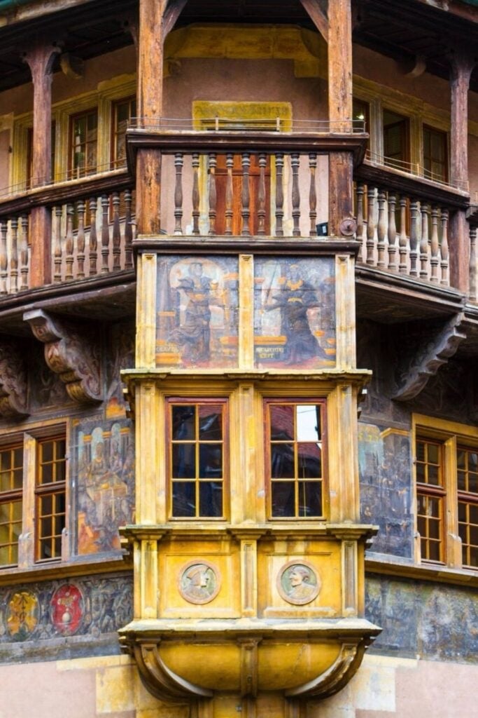 A close-up view of the historic Pfister House in Colmar, France, featuring its beautifully preserved wooden balconies and Renaissance-style frescoes. The intricate painted details and ornate bay windows make this 16th-century building a standout architectural gem. A must-see landmark when spending *one day in Colmar.