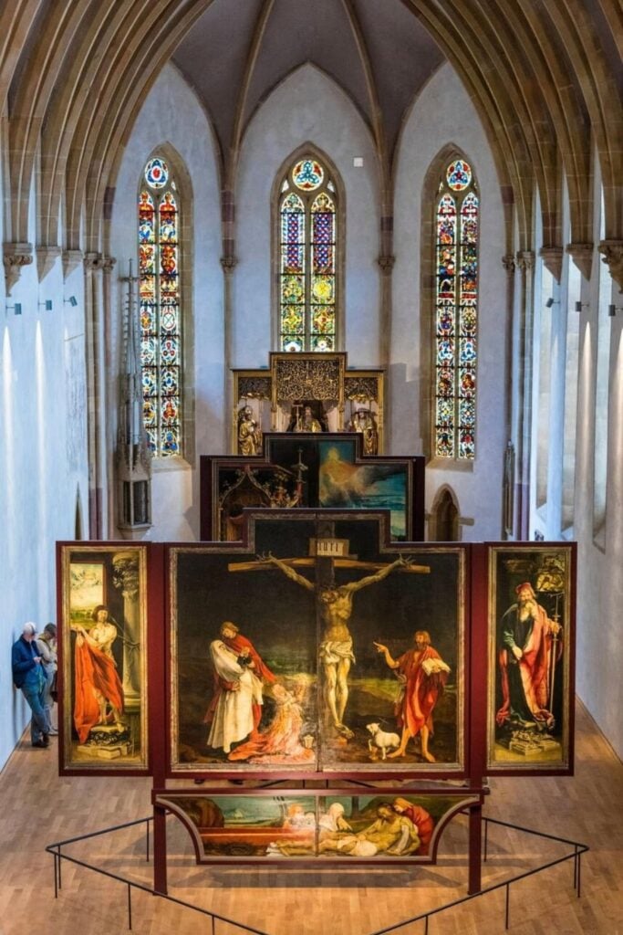 The stunning Isenheim Altarpiece displayed inside the Unterlinden Museum in Colmar, France. The grand Gothic-style hall features arched ceilings and intricate stained-glass windows, providing a breathtaking backdrop for this famous masterpiece. A must-see attraction for art lovers spending one day in Colmar.
