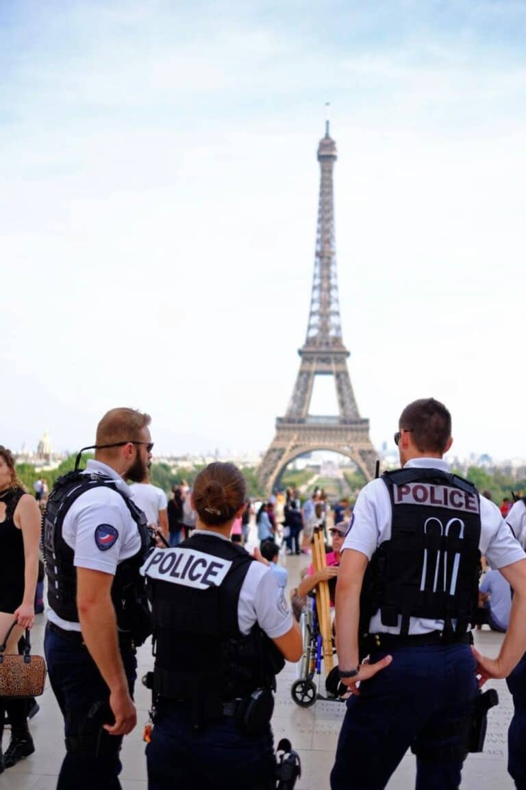 Police officers standing guard near the Eiffel Tower, a visible reminder of increased vigilance even in tourist hotspots, as part of broader efforts to monitor dangerous neighborhoods in Paris.