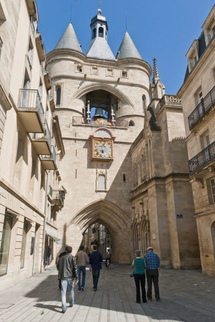 People walk toward the Grosse Cloche, a historic medieval gate with a striking bell and clock, making it a must-visit landmark for those exploring things to do in Bordeaux.