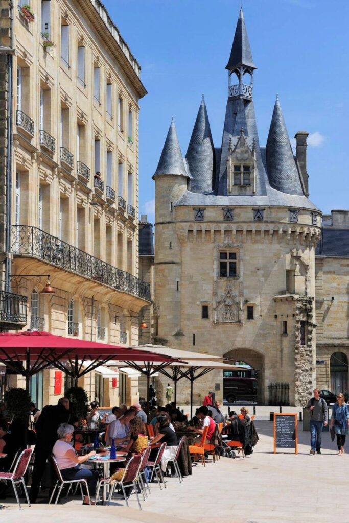 People enjoy outdoor dining at a lively café near Porte Cailhau, a stunning medieval gate that stands as a historic landmark and a must-see among the many things to do in Bordeaux.