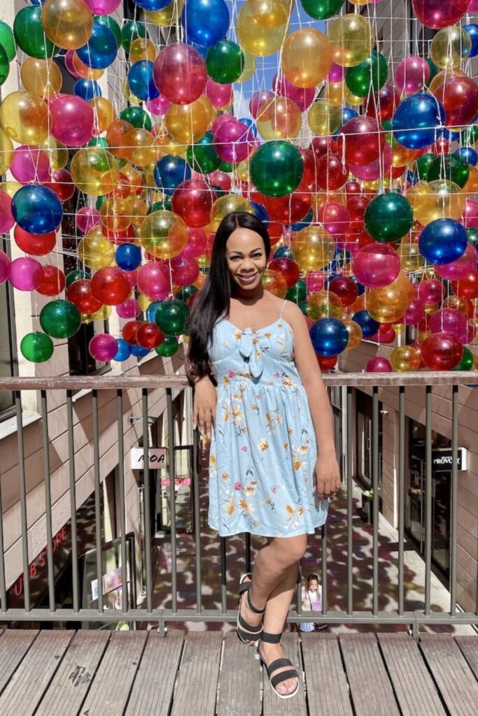 A woman poses in front of a vibrant floating balloon installation at Bordeaux’s Promenade Sainte-Catherine, a colorful and trendy spot that adds a unique twist to things to do in Bordeaux.