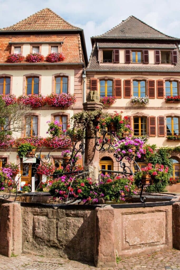 Flower-filled fountain in the charming village of Bergheim, one of the most delightful places to visit in Alsace, known for its picturesque streets and colorful buildings.