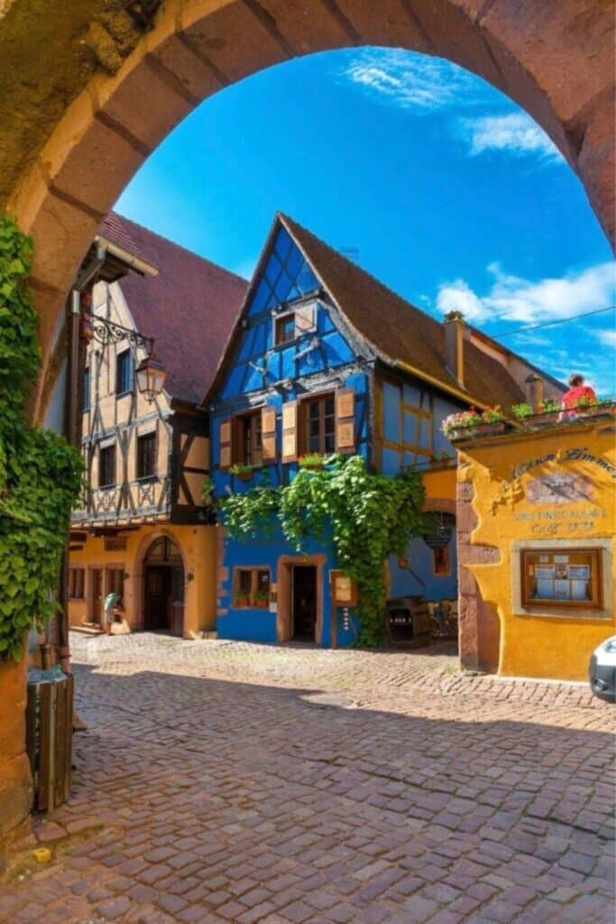 Charming view of Riquewihr, a vibrant village in Alsace with colorful half-timbered houses, nestled under an archway, making it a top place to visit in Alsace.