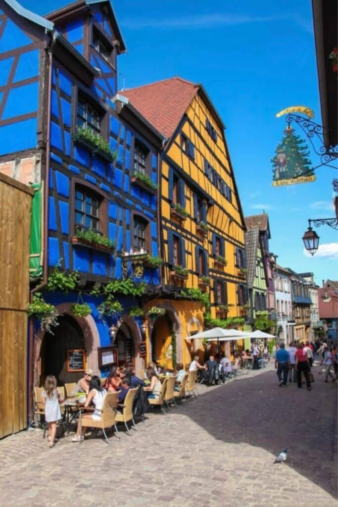 Colorful half-timbered houses and outdoor cafés in Riquewihr, one of the most vibrant places to visit in Alsace, where you can enjoy scenic streets and local culture.