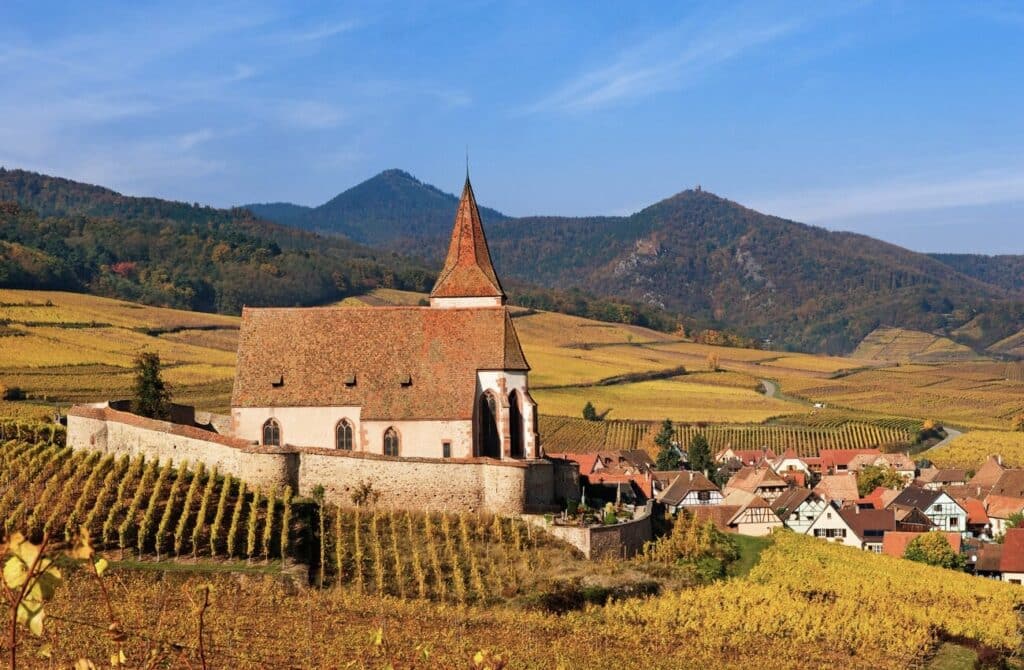 Stunning view of the church in Hunawihr, surrounded by vineyards and the Vosges mountains, making it one of the scenic places to visit in Alsace