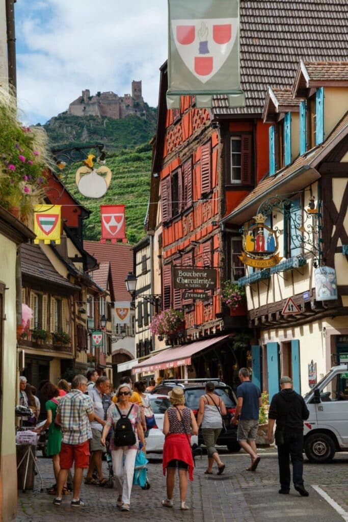 Charming street view in Kaysersberg, with colorful timber-framed houses and the Château de Kaysersberg in the background, one of the most picturesque places to visit in Alsace.