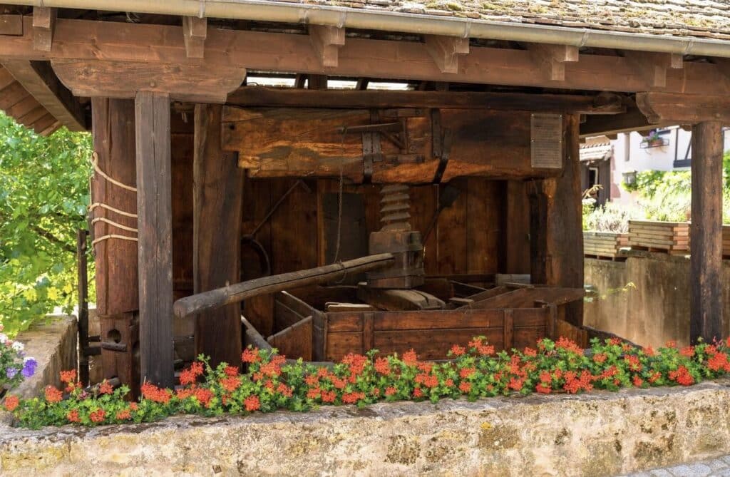 Historic wine press in Mittelbergheim, a charming place to visit in Alsace, surrounded by vibrant flowers, reflecting the region's rich winemaking heritage.