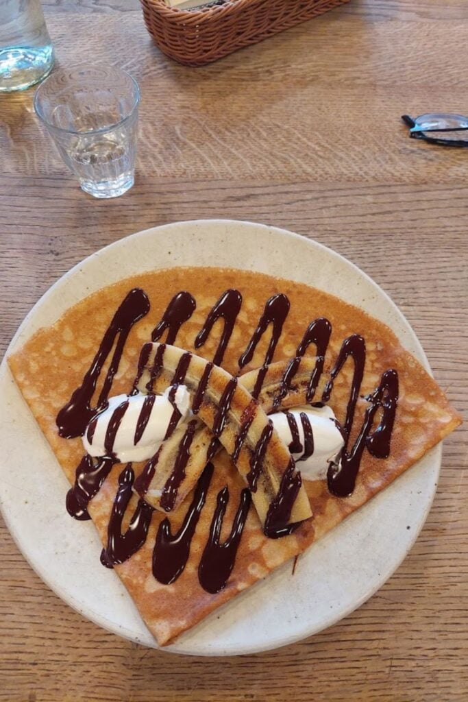 A decadent crêpe topped with whipped cream, chocolate drizzle, and crushed nuts, paired with an espresso, epitomizing the best crêpes in Paris.