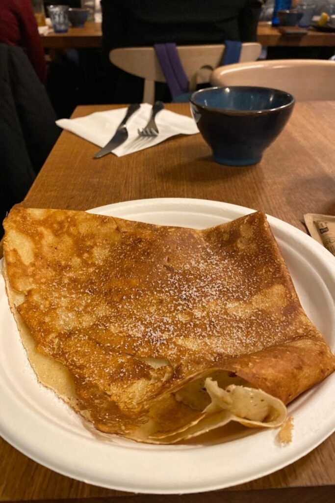 A simple yet delicious butter and sugar crêpe served on a paper plate, capturing the charm of the best crêpes in Paris.