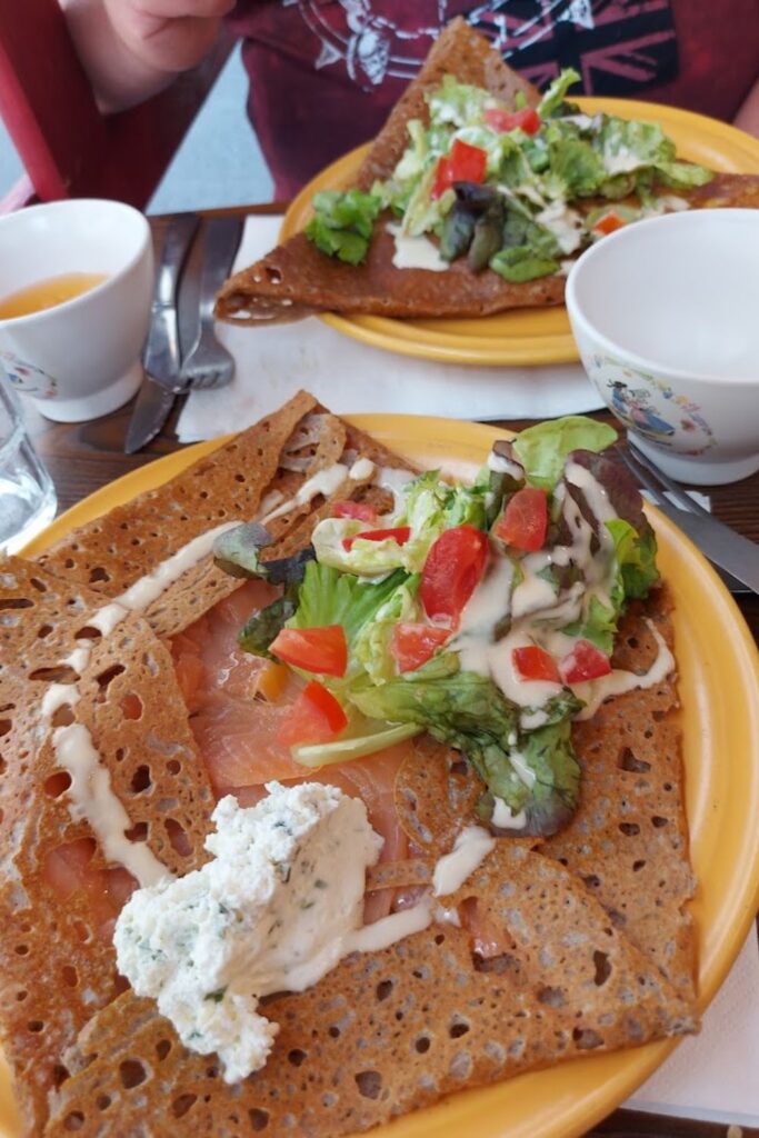 A savory buckwheat crêpe topped with smoked salmon, fresh salad, creamy dressing, and a dollop of herb cheese, showcasing the best crêpes in Paris.