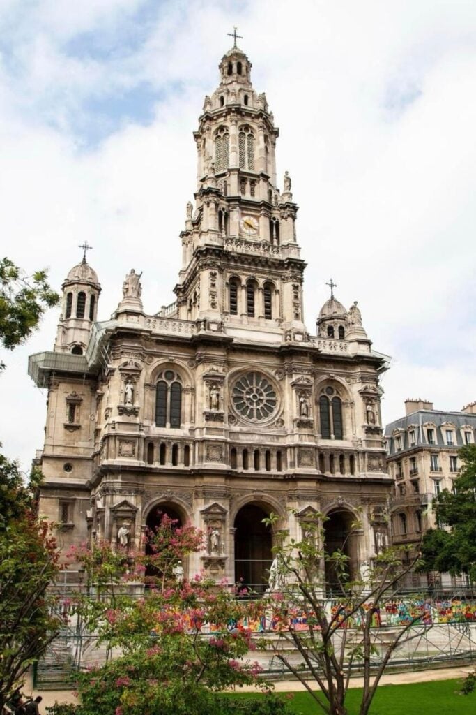 A frontal view of the Église de la Sainte-Trinité in the 9th arrondissement of Paris, showcasing its ornate architecture, tall bell tower, and colorful flowers in the foreground.