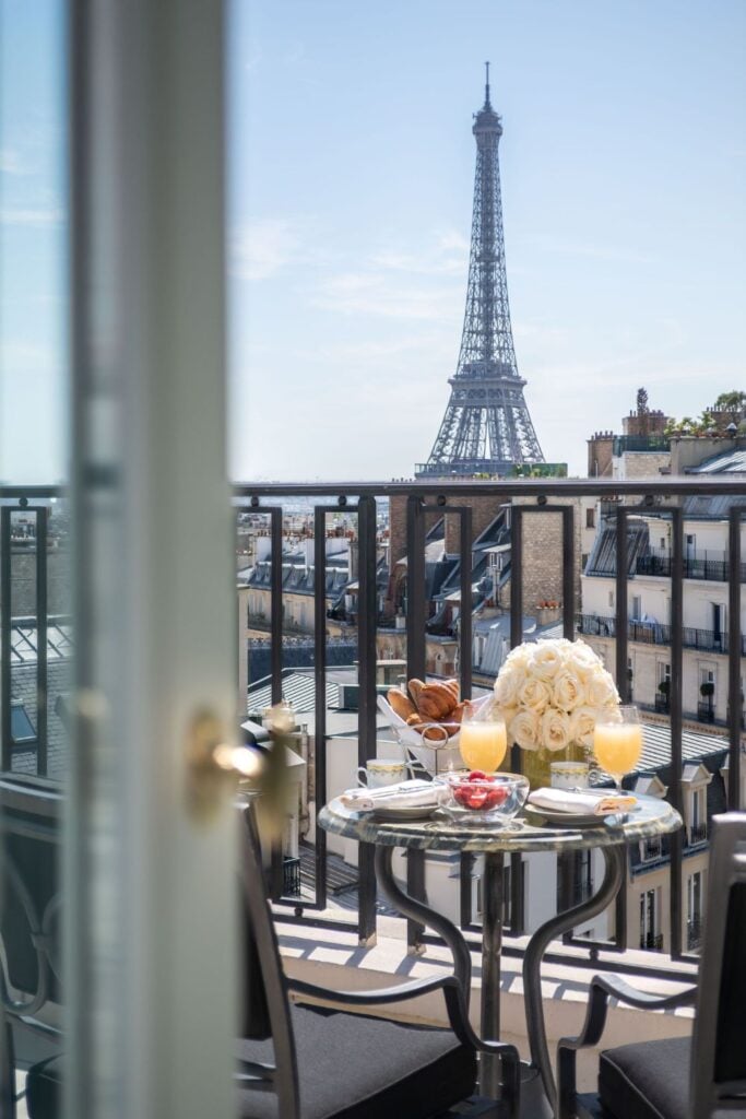 An elegant balcony breakfast with croissants, fruit, and orange juice, complemented by a breathtaking Eiffel Tower backdrop, ideal for Paris hotels with Eiffel Tower views.