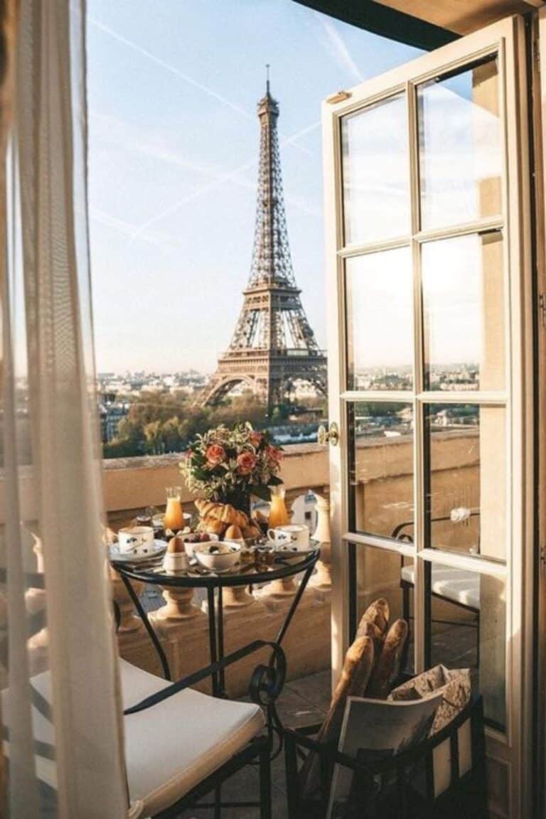 A charming balcony breakfast setup with croissants, flowers, and juice, overlooking the Eiffel Tower, highlighting Paris hotels with Eiffel Tower views.