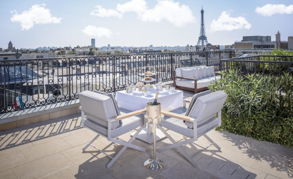 A luxurious rooftop terrace with elegant seating, a table set for dining, and a breathtaking view of the Eiffel Tower, showcasing the allure of Paris hotels with Eiffel Tower views.