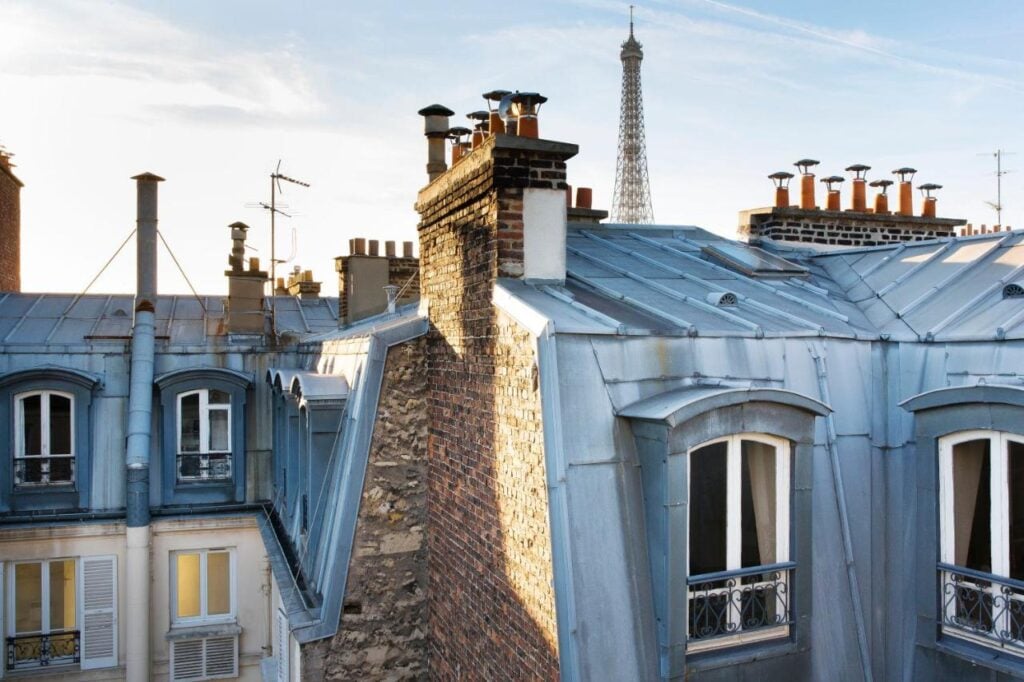 Rooftop view from Cler Hotel showing classic Parisian zinc rooftops with chimneys and a distant view of the Eiffel Tower, ideal for cheap hotels with Eiffel Tower view.