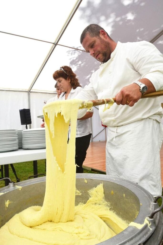 A chef stretches a large pot of aligot, a creamy and elastic mashed potato dish blended with cheese, showcasing the indulgent textures of traditional French foods.