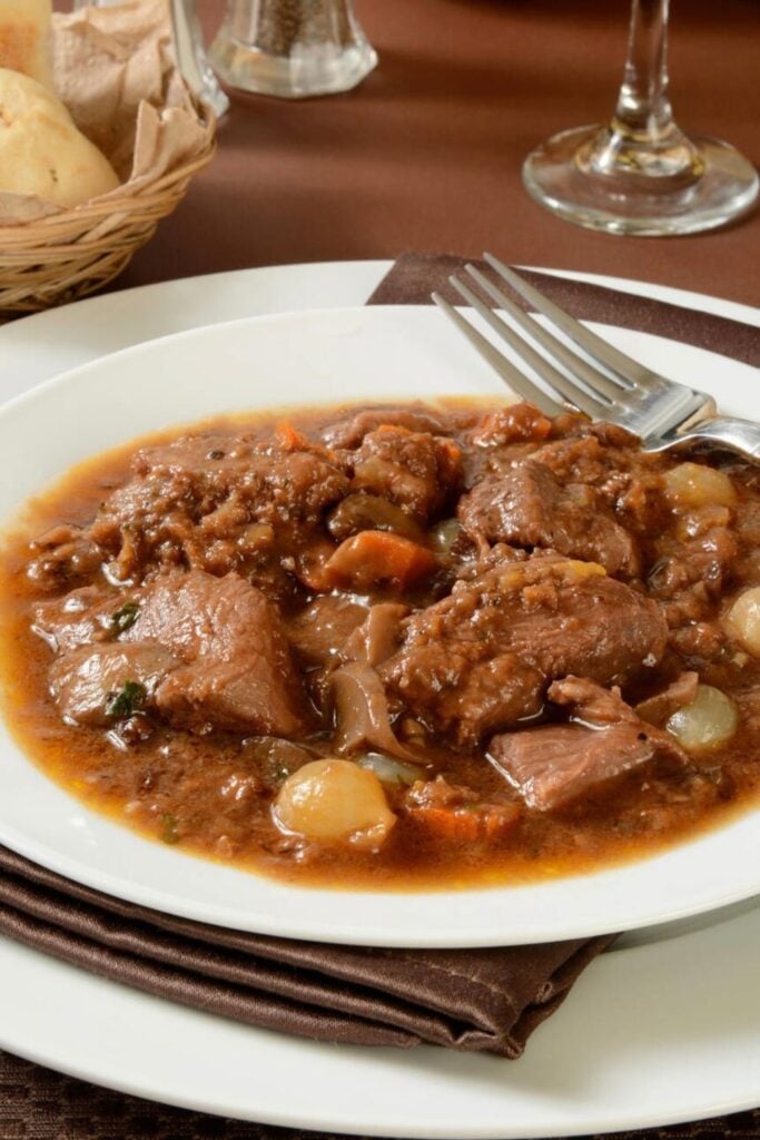 A plate of rich and savory boeuf bourguignon, a classic traditional French foods, featuring tender beef slow-cooked in red wine with onions, mushrooms, and carrots.