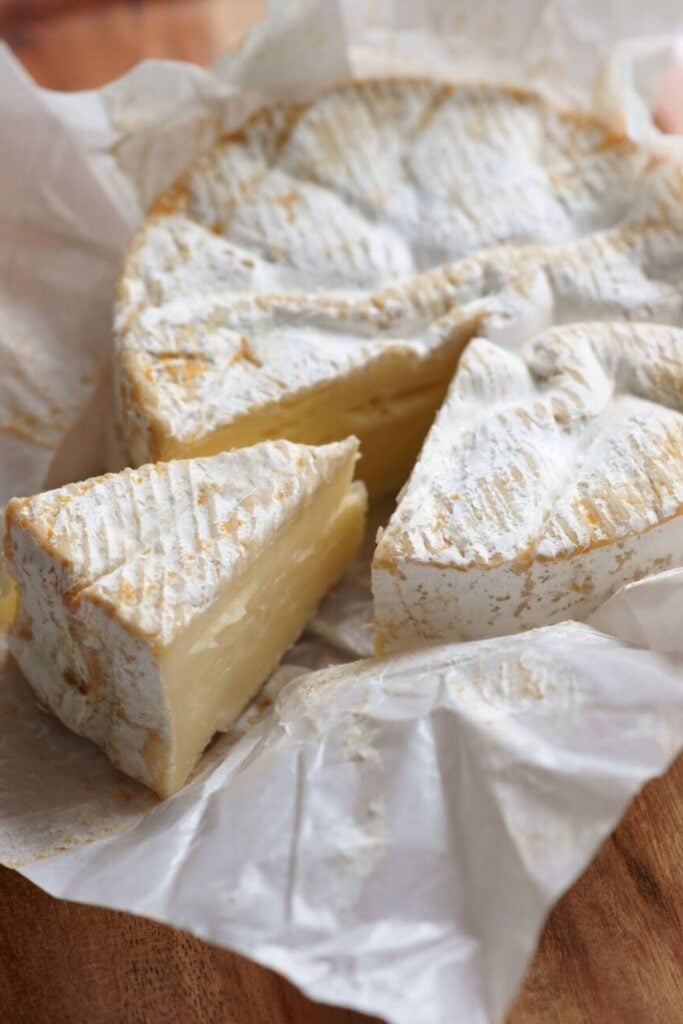 A wheel of creamy Camembert cheese with a bloomy rind, partially sliced to reveal its soft interior, representing the rich flavors of traditional French foods.