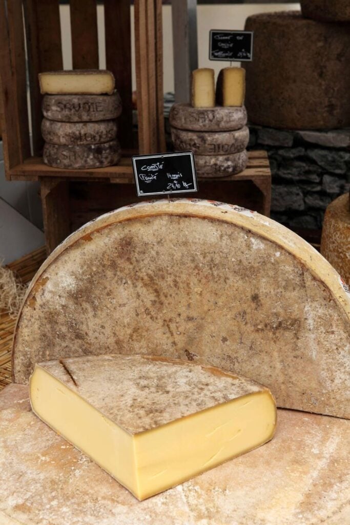 A rustic wheel of Comté cheese, a beloved traditional French foods, with a firm, golden interior and aged rind, displayed at an artisanal market.