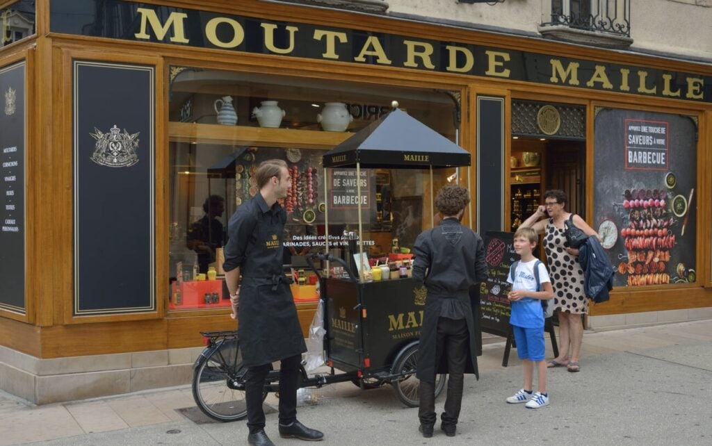 A charming mustard boutique, Maison Maille in Paris, offers gourmet mustard tastings from a street cart, a delightful stop for food lovers on day trips from Paris France.