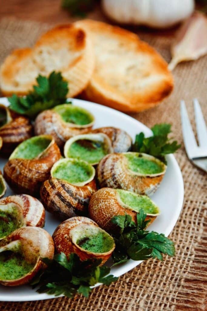 A plate of escargots de Bourgogne, a classic traditional French foods featuring snails baked in garlic and parsley butter, served with toasted bread.